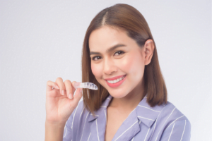 Smiling woman holds clear dental aligners